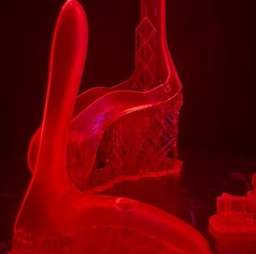 Abstract, translucent 3D-printed objects illuminated by bright red light, with smooth, curved shapes and intertwined lattice beams against a dark background.