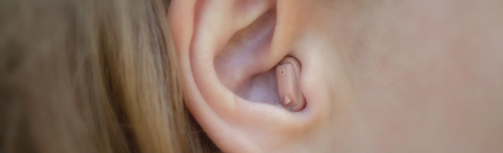 Close-up of a persons ear with a small, flesh-colored hearing aid device inserted in the ear canal.